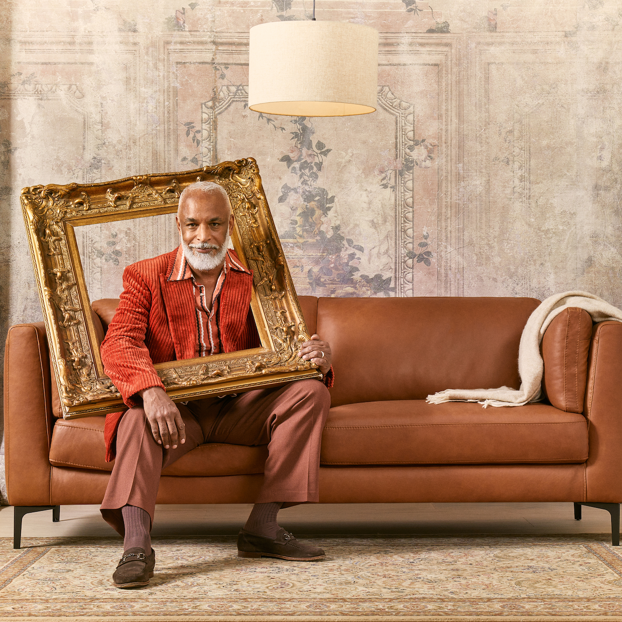 A stylish man relaxes on a luxurious leather sofa, holding a beautiful frame with care.